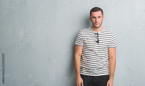 Young caucasian man over grey grunge wall skeptic and nervous, frowning upset because of problem. Negative person.