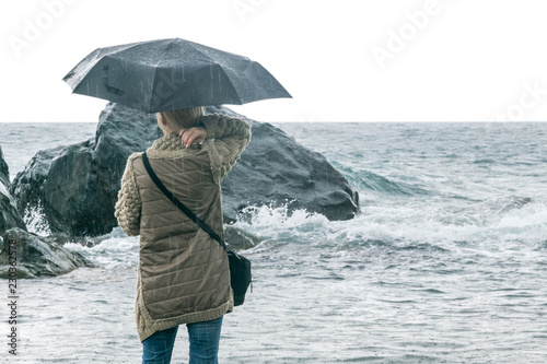 Female depression, loneliness concept. The woman is under an umbrella in the rain against the backdrop of stones and the exciting sea.