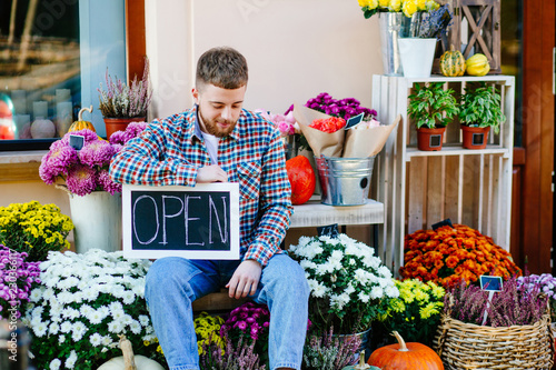 Business man owner holding open sign at workplace near his flower shop with autumn outdoor colorful store dercoration. photo