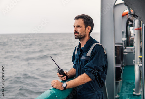 Marine Deck Officer or Chief mate on deck of vessel or ship . He holds VHF walkie-talkie radio in hands. Ship communication photo