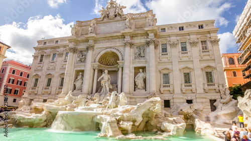tourists and people walking next to the Trevi Fountain in a sunny day with clouds, one of the most famous fountain in the world. Rome, Lazio, Italy.