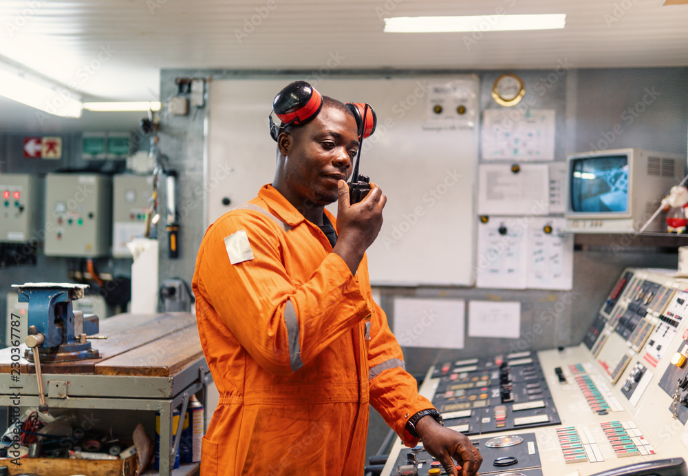 African marine engineer officer in engine control room ECR. He speaks with VHF or UHF portable radio. Ship communication routine African marine engineer officer in engine control room ECR. He speaks with VHF or UHF portable radio. Ship communication routine
