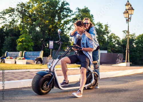 Lovely young couple dating with electric bike. Modern city life and transportation. She closes his eyes photo