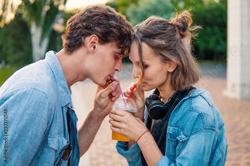 Lovely young hipster couple dating during summer sunset. they wear jeans clothes. They drink one cocktail together