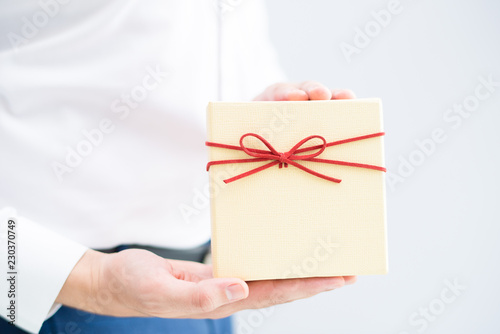 Closeup of person holding gift box. Man showing gift box. Gift concept. Isolated cropped view on grey background. © Mangostar