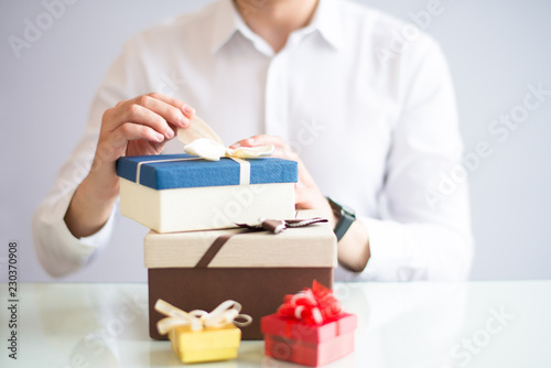 Closeup of person unwrapping gifts. Person sitting at table. Gifts concept. Cropped view. photo