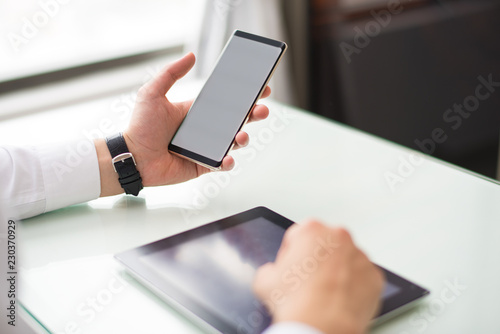 Closeup of person using smartphone and tablet computer at table. Digital gadgets. Technology and communication concept. Cropped view.