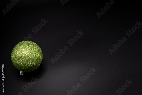 Green glittered christmas ball on black background. Copy space.