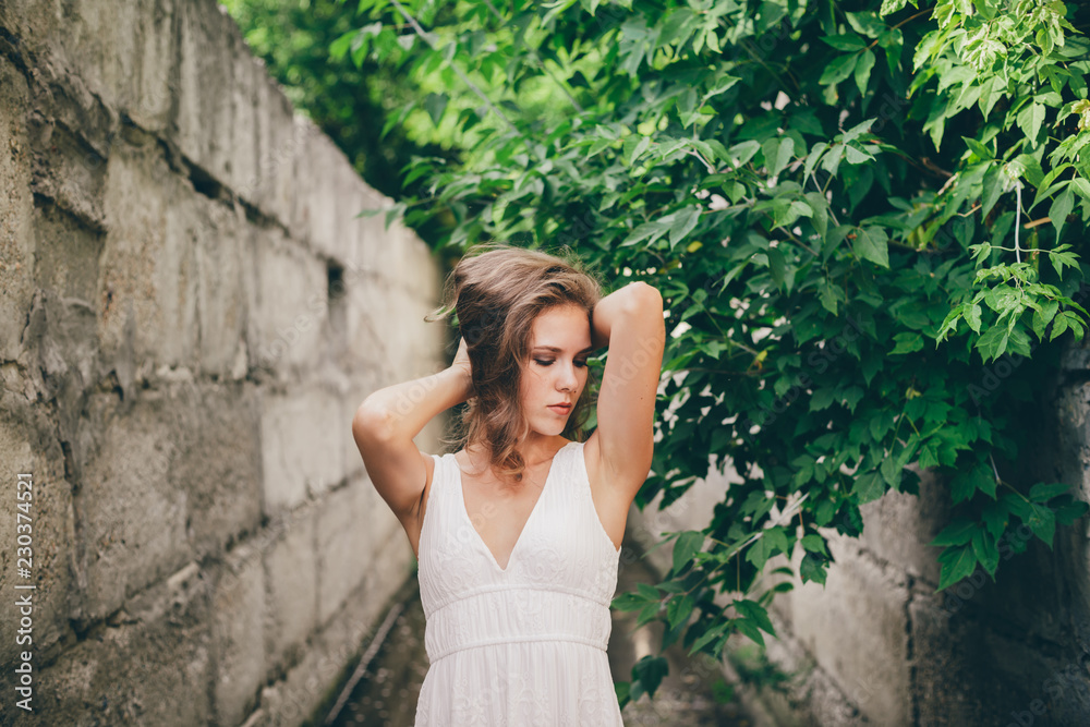 Beautiful happy girl with curly natural hair in white dress near green tree leaves. Summer beauty portrait. Dreamer lady enjoy nature. Inspired woman with dreamy sight in long tunnel in forest.