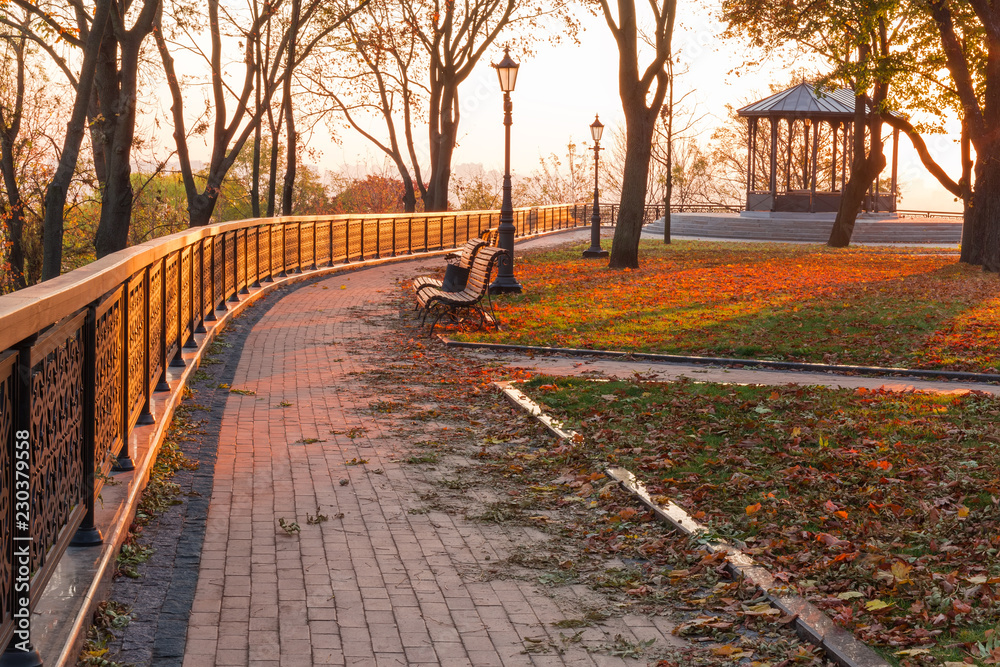 Alley with fence, benches and street lights in autumn park