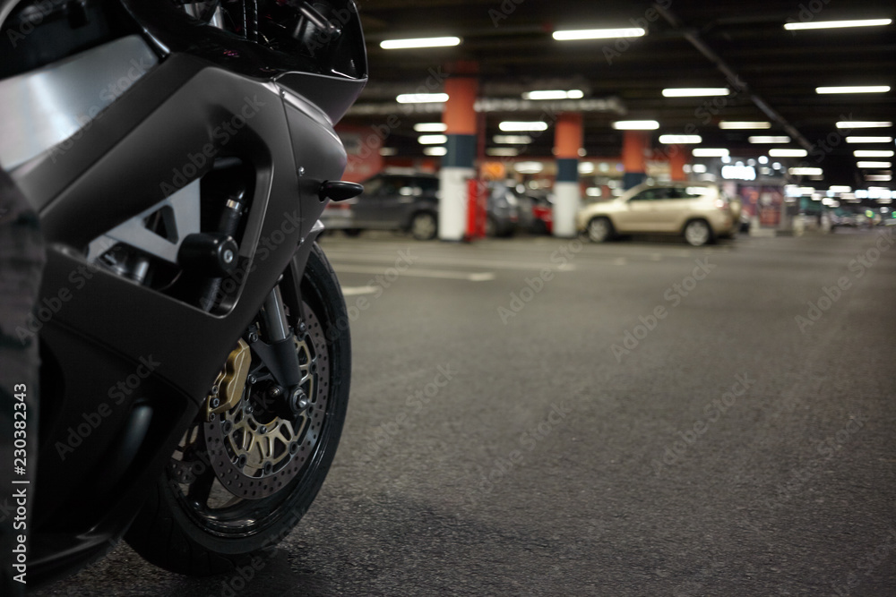 Cropped shot of blue motorbike in underground parking lot with cars parked in background. Close up of motorcycle rear tyre, blank asphalt with copy space for your text or promotional content