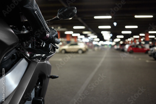 Cropped shot of stylish new motorcycle with female arm in black leather jacket driving sportbike on underground garage or car parking with blank copyspace concrete floor for your text or advertisement