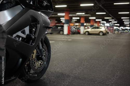 Cropped shot of blue motorbike in underground parking lot with cars parked in background. Close up of motorcycle rear tyre, blank asphalt with copy space for your text or promotional content photo
