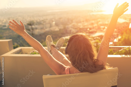 Girl with a long hair on the chair on the balcony on the sunset town background
