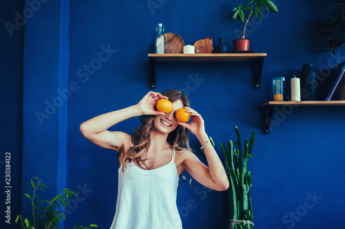 Young woman on a blue background holds a cut orange in her hands and laughs. Colour obsession concept. 