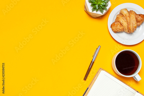 Cup of coffee, open notebook with blank pages, fresh croissant, cactuses succulents on yellow blue minimalistic background, top view Flat Lay with copy space. Empty office desk, Still life, business