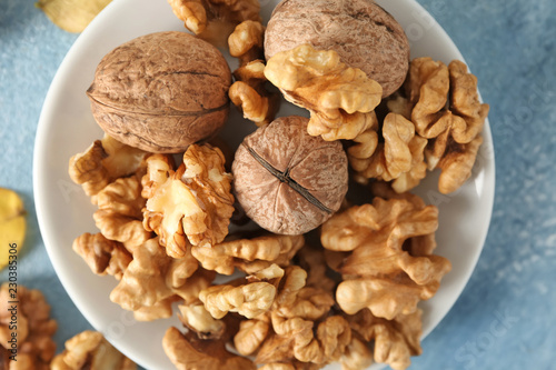 Plate with tasty walnuts on color table, closeup