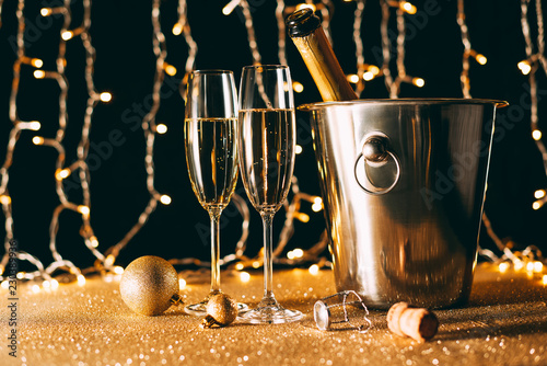 two glasses and champagne bottle in bucket on garland light background, christmas concept
