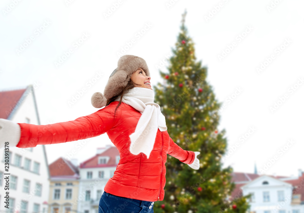 Obraz premium people, season and leisure concept - happy woman in winter fur hat over christmas tree at tallinn old town hall square background