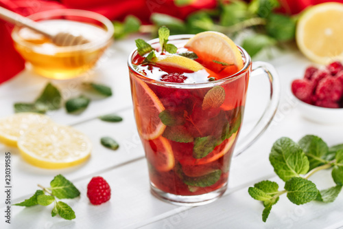 Red hot tea with raspberry on white wooden background. Decorated with mint leaves, lemon and honey