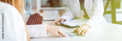 A beautiful young girl in a white robe is sitting at the desk in the office and communicating with the interlocutor. The interlocutor gives the girl money.