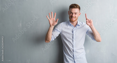 Young redhead business man over grey grunge wall showing and pointing up with fingers number six while smiling confident and happy.