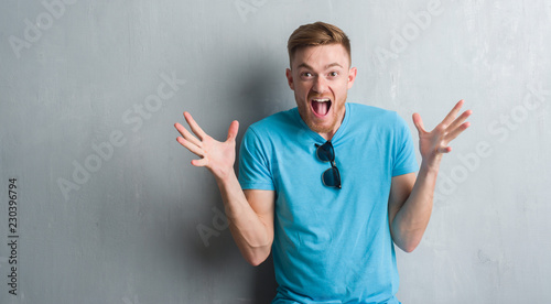 Young redhead man over grey grunge wall wearing casual outfit celebrating crazy and amazed for success with arms raised and open eyes screaming excited. Winner concept