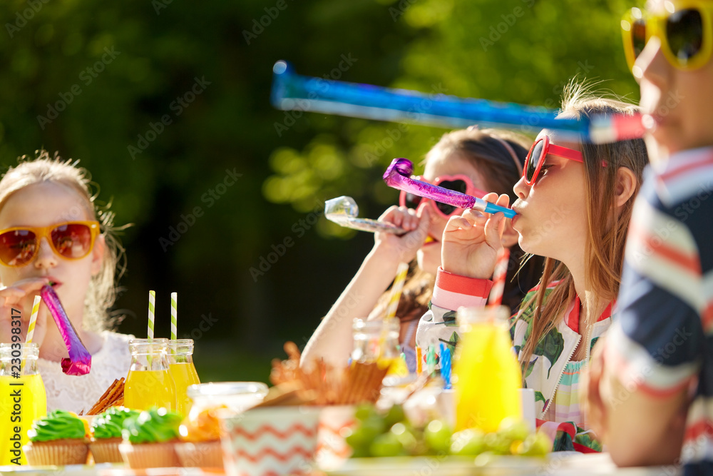 birthday, childhood and celebration concept - close up of happy kids blowing party horns and having fun in summer