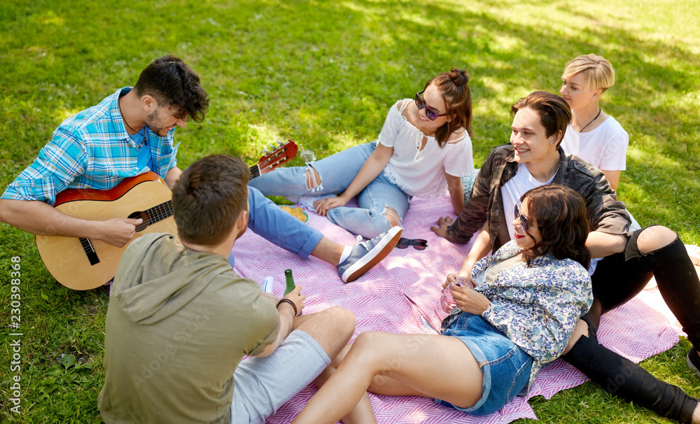 friendship, leisure and summer concept - group of happy smiling friends with guitar and non alcoholic drinks chilling on picnic blanket at summer park friendship, leisure and summer concept - group of happy smiling friends with guitar and non alcoholic drinks chilling on picnic blanket at summer park
