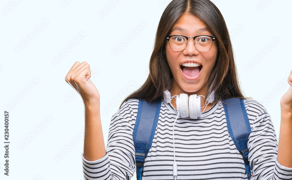 Young asian student woman wearing headphones and backpack over isolated background celebrating surprised and amazed for success with arms raised and open eyes. Winner concept. Young asian student woman wearing headphones and backpack over isolated background celebrating surprised and amazed for success with arms raised and open eyes. Winner concept.