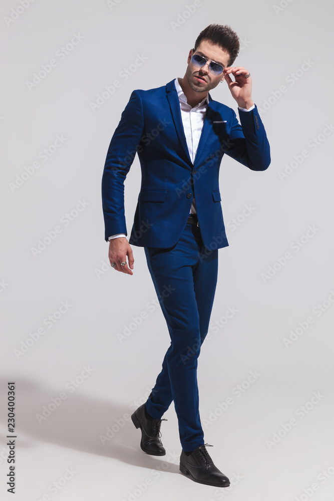 elegant man walks and fixes his sunglasses while looking away elegant man walks and fixes his sunglasses while looking away