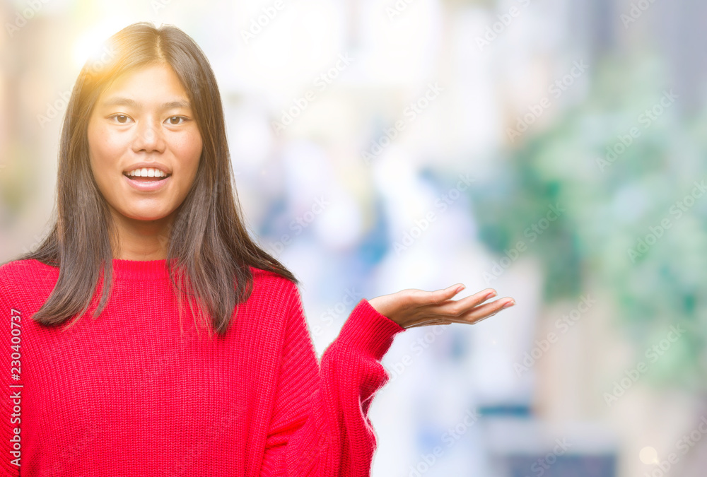 Young asian woman wearing winter sweater over isolated background smiling cheerful presenting and pointing with palm of hand looking at the camera.