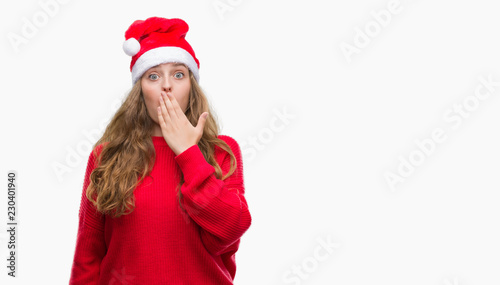 Young blonde woman wearing santa claus hat cover mouth with hand shocked with shame for mistake, expression of fear, scared in silence, secret concept