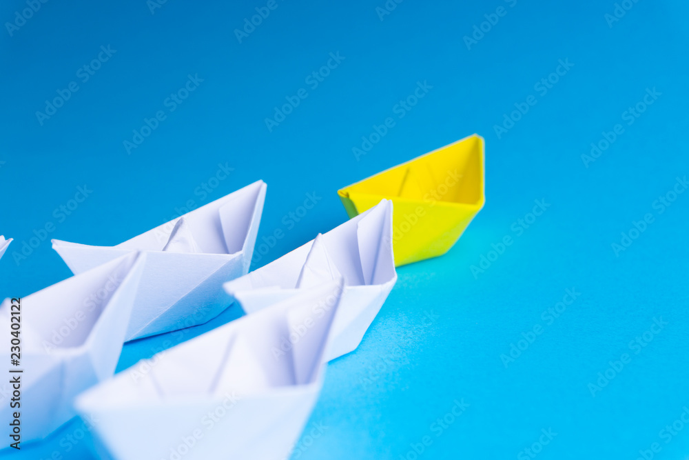 Naklejka premium White and yellow paper boat or ship in one direction on blue background. Business for innovative solution concept with selective focus