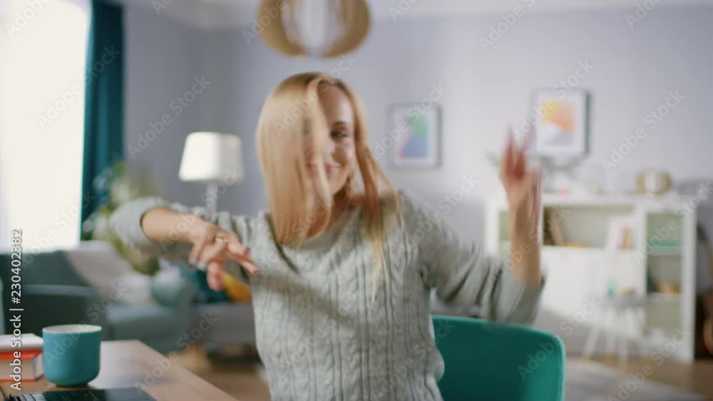 Beautiful Cheerful Blonde Does Funny Dance Routine while Sitting at Her Desk in the Living Room. Happy Woman Doing Celebratory Dancing. Beautiful Cheerful Blonde Does Funny Dance Routine while Sitting at Her Desk in the Living Room. Happy Woman Doing Celebratory Dancing.