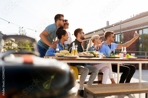 leisure and people concept - happy friends with drinks having barbecue party on rooftop in summer and taking selfie by smartphone © Syda Productions