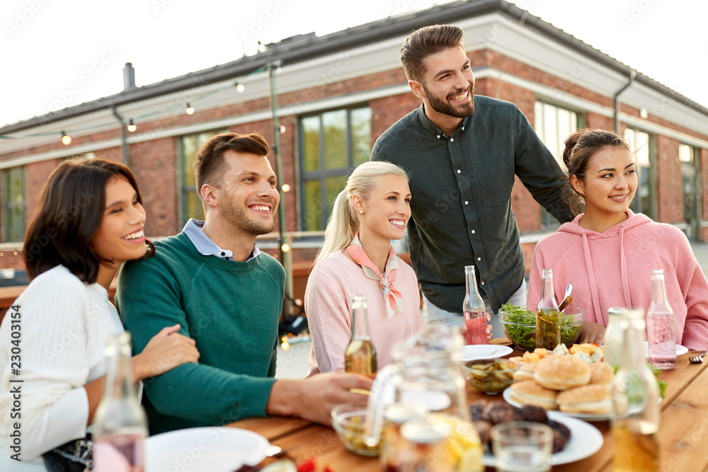 Obraz premium leisure and people concept - happy friends with drinks having barbecue party on rooftop