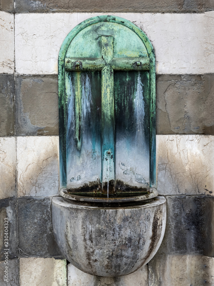 fountain in a cemetery for the supply of drinking water decorated with a bronze plate depicting a crucifix.Milan, Italy fountain in a cemetery for the supply of drinking water decorated with a bronze plate depicting a crucifix.Milan, Italy