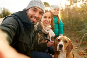 family, pets and people concept - happy mother, father and little daughter with beagle dog taking selfie outdoors in autumn