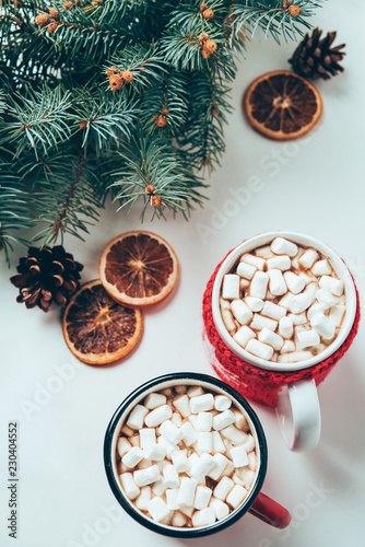 top view of cups of hot chocolate with marshmallows and pine tree branches on white surface, christmas breakfast concept