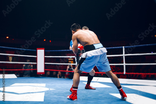 Two professional boxers, athletes in dynamic boxing action on the ring under lights of sport arena
