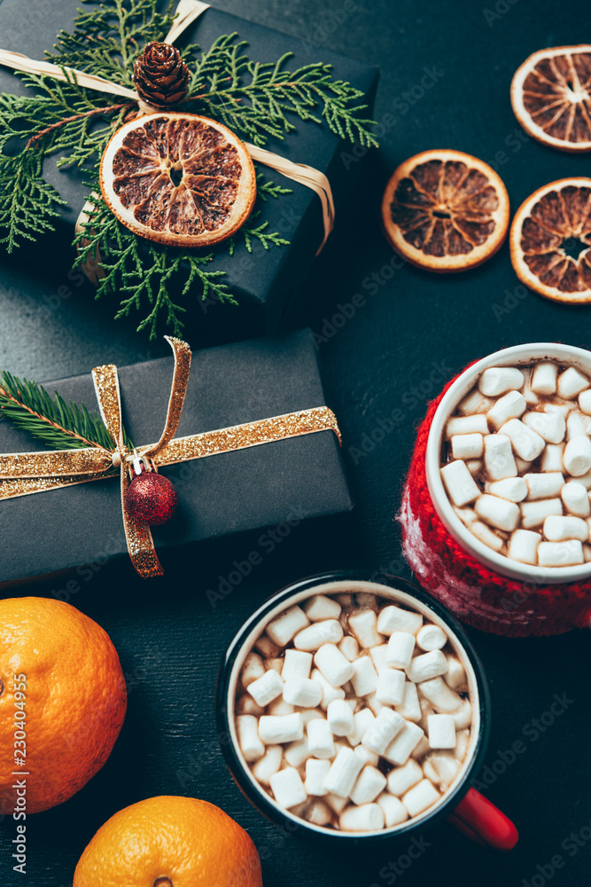 top view of cups of hot drinks with marshmallows, tangerines and christmas presents on black surface top view of cups of hot drinks with marshmallows, tangerines and christmas presents on black surface