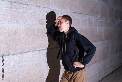 Upset teenager leaning against the brick wall of a high school at night.