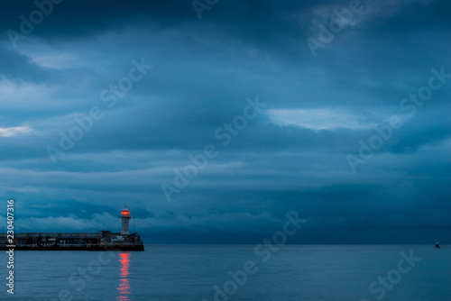 Beautiful lighthouse on the seashore at dusk, rainy clouds over the sea