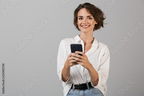 Happy young business woman posing using mobile phone chatting.