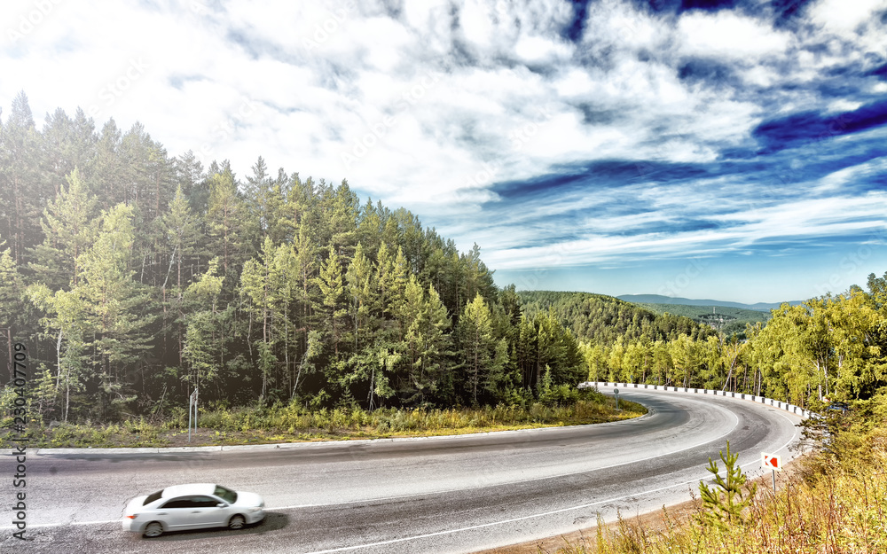 Scenic panorama scenery overview of taiga forest mountain road leading through green trees with white car on foreground beautiful sloppy hills background russia siberia nature travel tourism theme