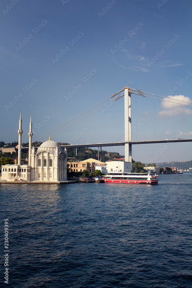View of old, historical Ortakoy Mosque by Bosphorus, tour boat, bridge and European side of Istanbul.