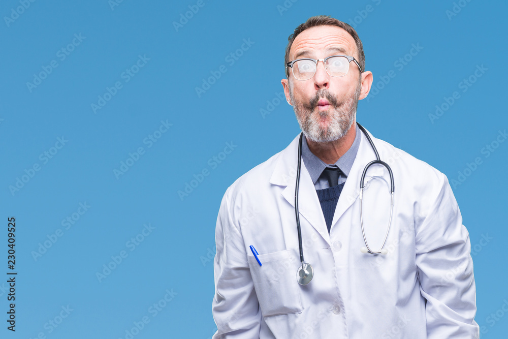 Middle age senior hoary doctor man wearing medical uniform isolated background making fish face with lips, crazy and comical gesture. Funny expression. Middle age senior hoary doctor man wearing medical uniform isolated background making fish face with lips, crazy and comical gesture. Funny expression.