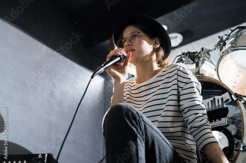 Low angle portrait of beautiful young woman singing to microphone during band rehearsal in studio, copy space