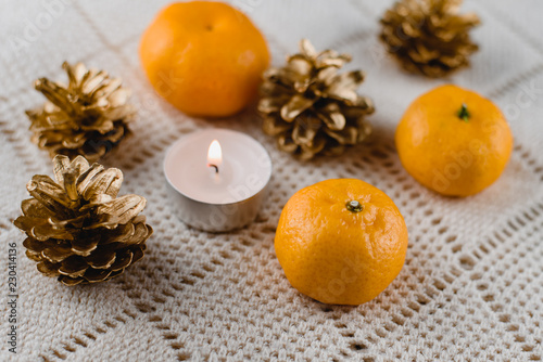 Christmas composition of mandarins , golden cones and a burning decorative candle on a light background